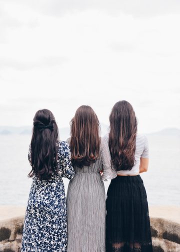 three woman looking back and facing body of water