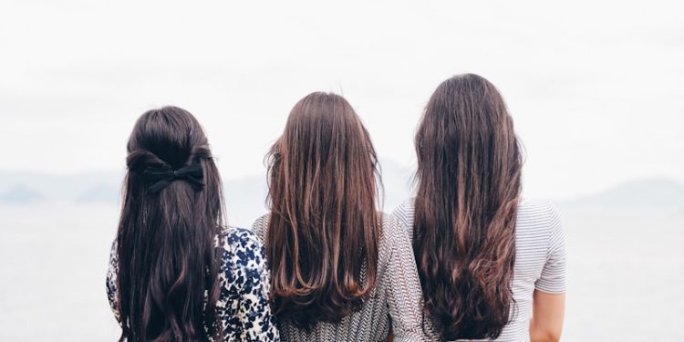 three woman looking back and facing body of water