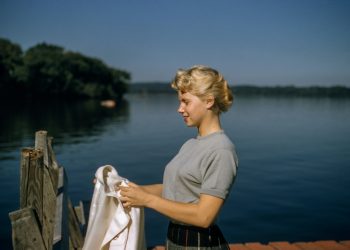woman holding white textile standing beside body of water