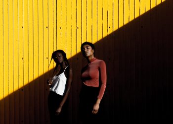 two women standing in front of yellow wall