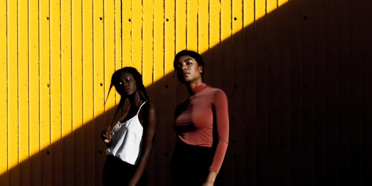 two women standing in front of yellow wall