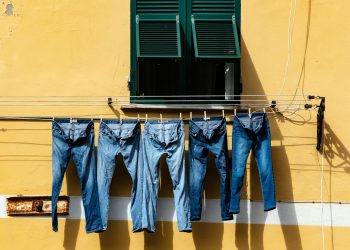 five blue denim jeans hanged on grey cable near window